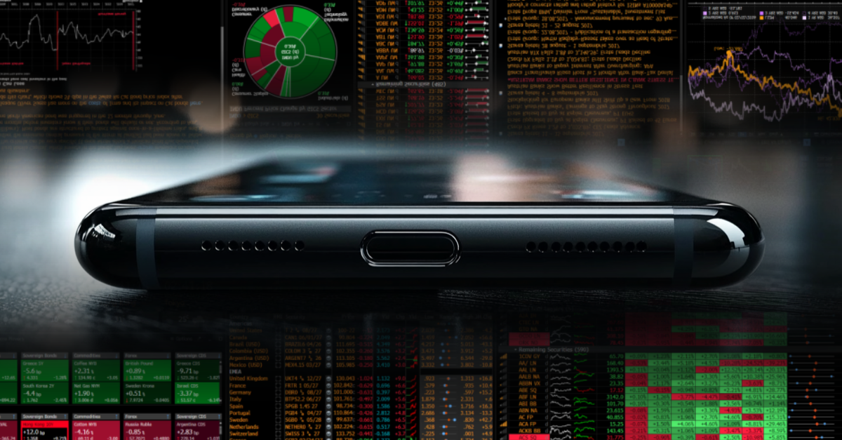iPhone with a trader's desktop screen in the background