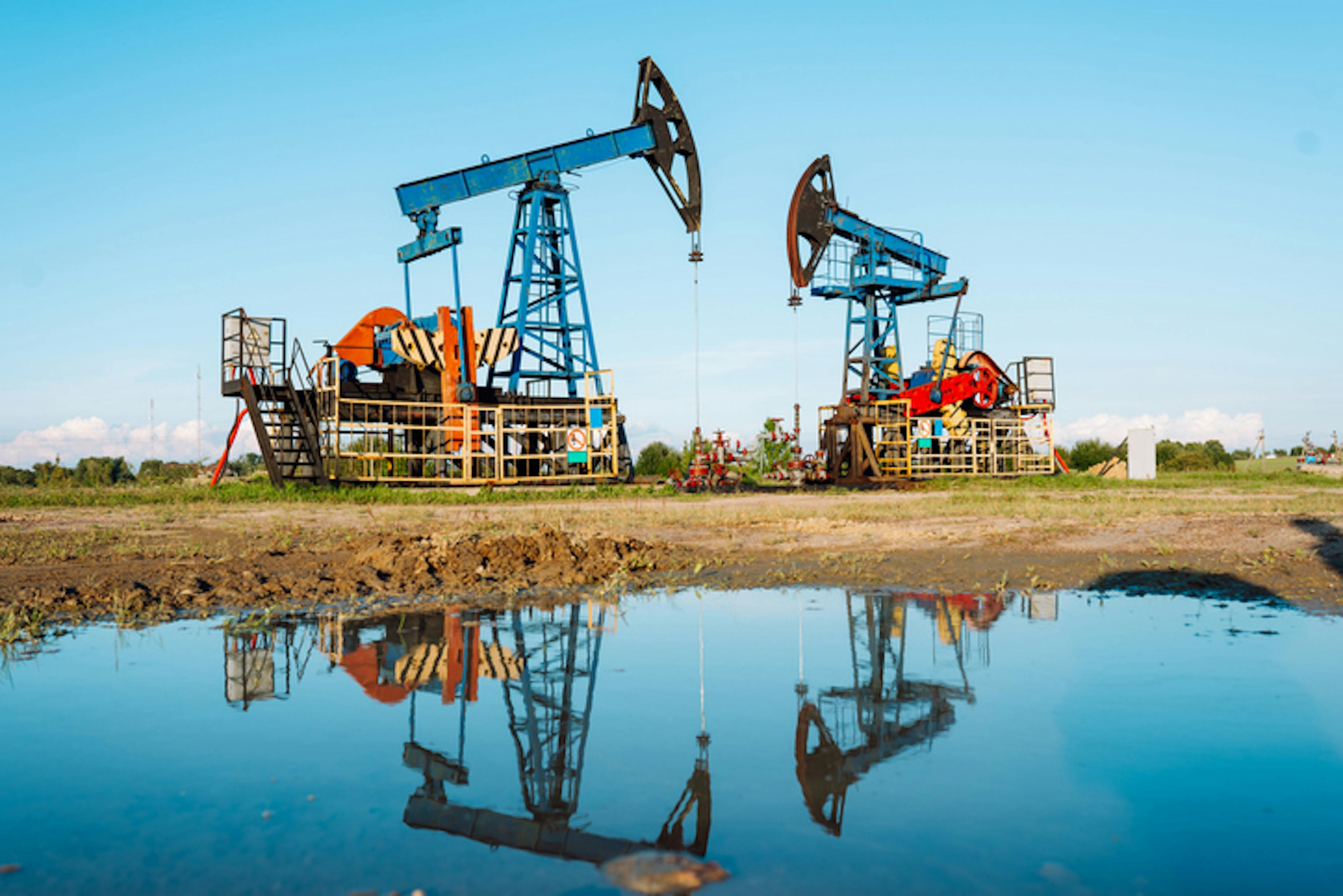 "Two pump jacks working near groundwater outlet with reflection in the puddle"