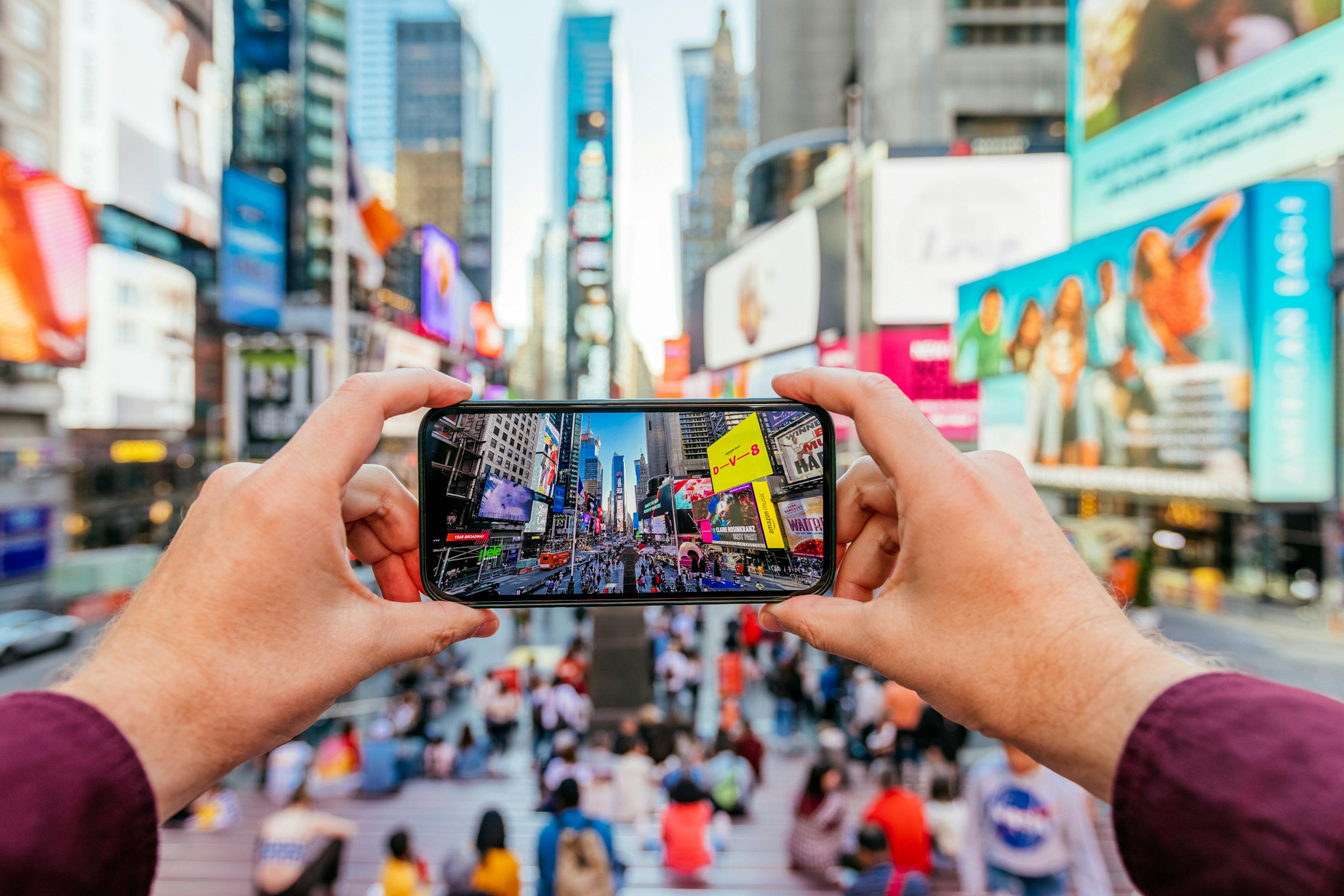 Man taking picture of Times Square using smart phone, personal perspective view