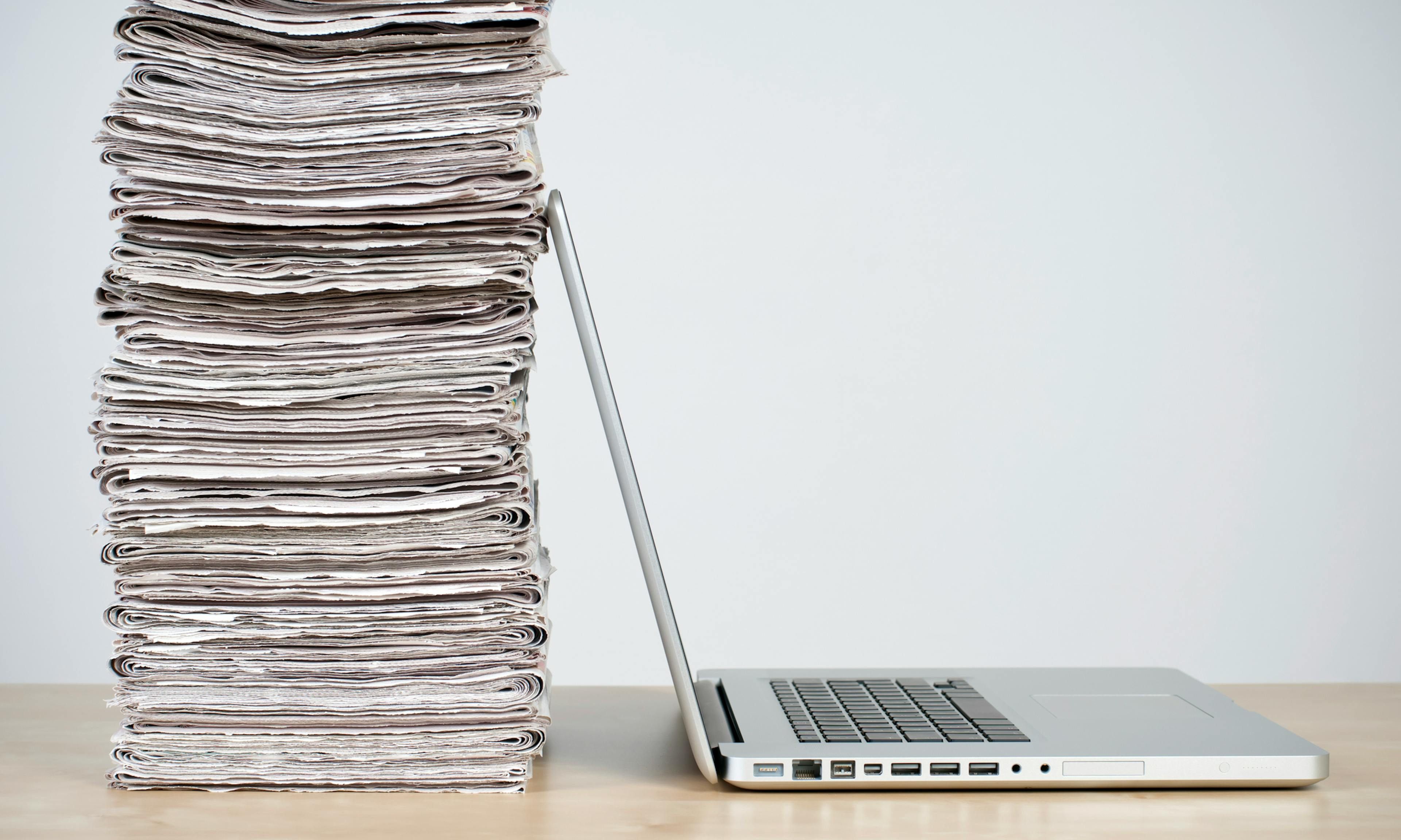Newspapers stacked up against a laptop
