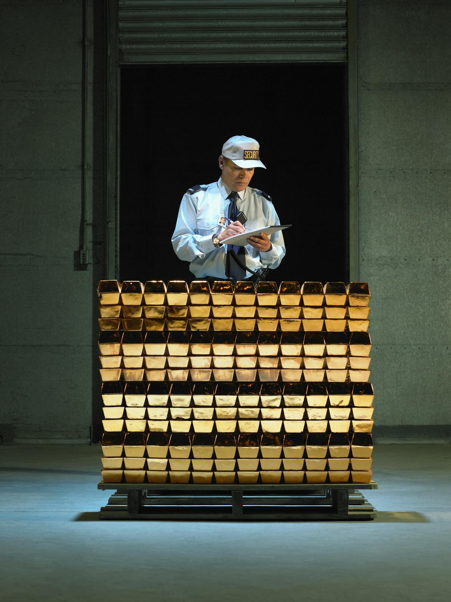 Security guard with clipboard and pen by stack of gold bars