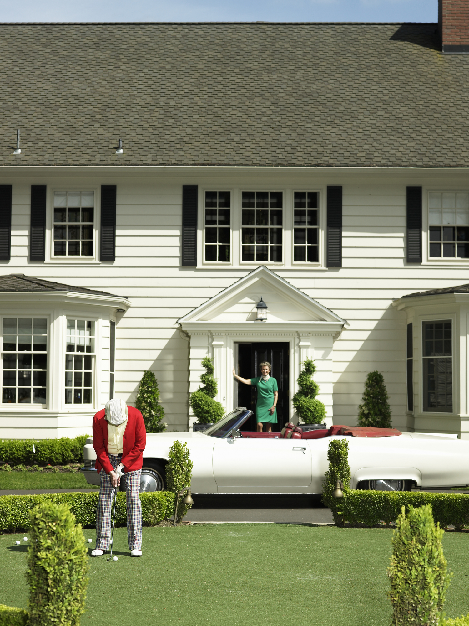 Senior man playing golf in front garden by convertible car