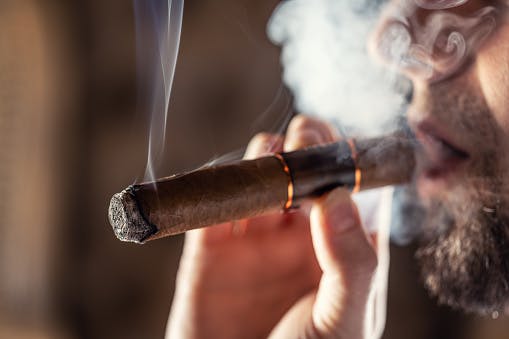 A young man smokes a Cuban cigar in a pub.