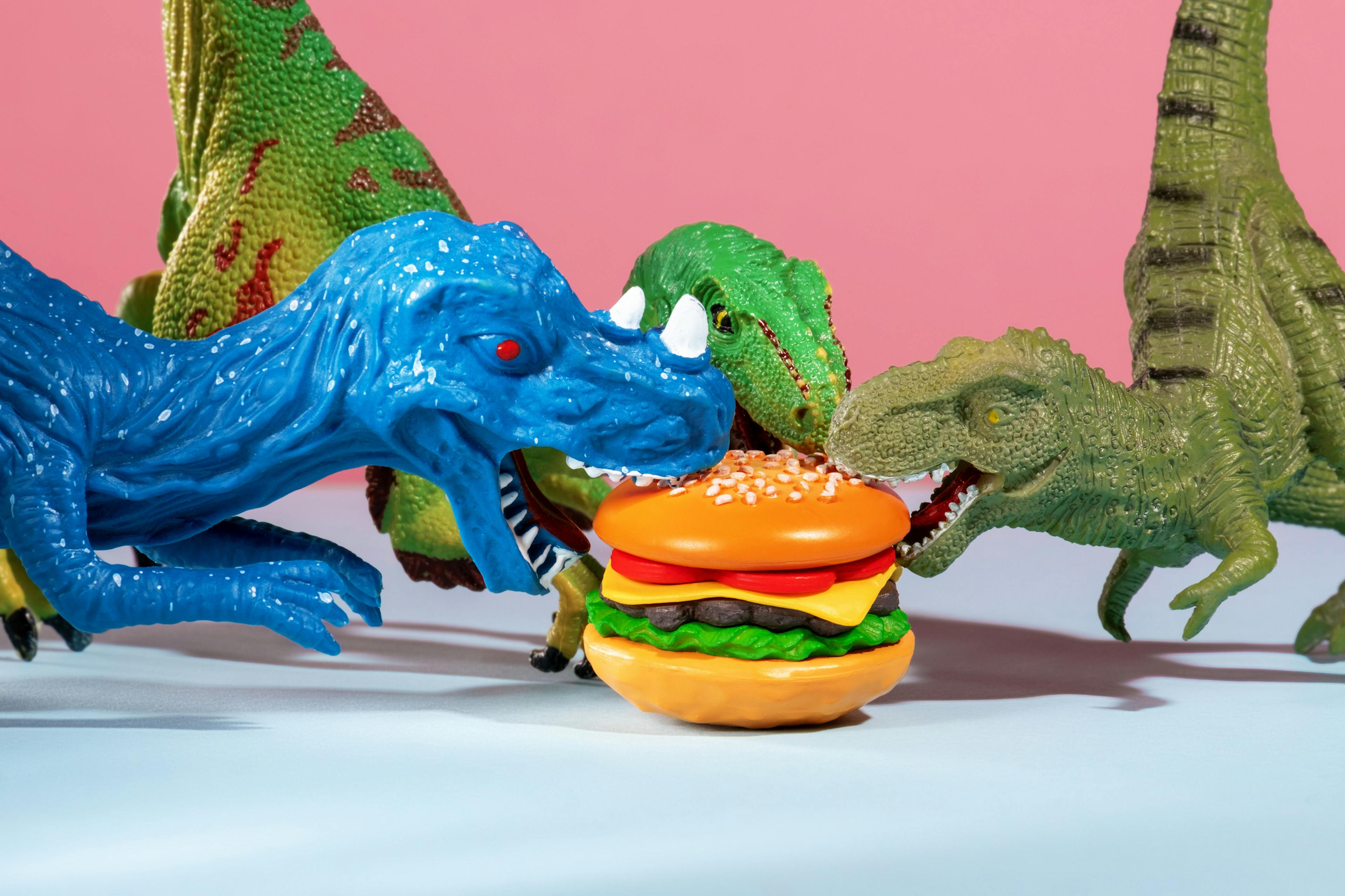 Three cute dinosaurs are fighting over burger. Humor and fast food concept.