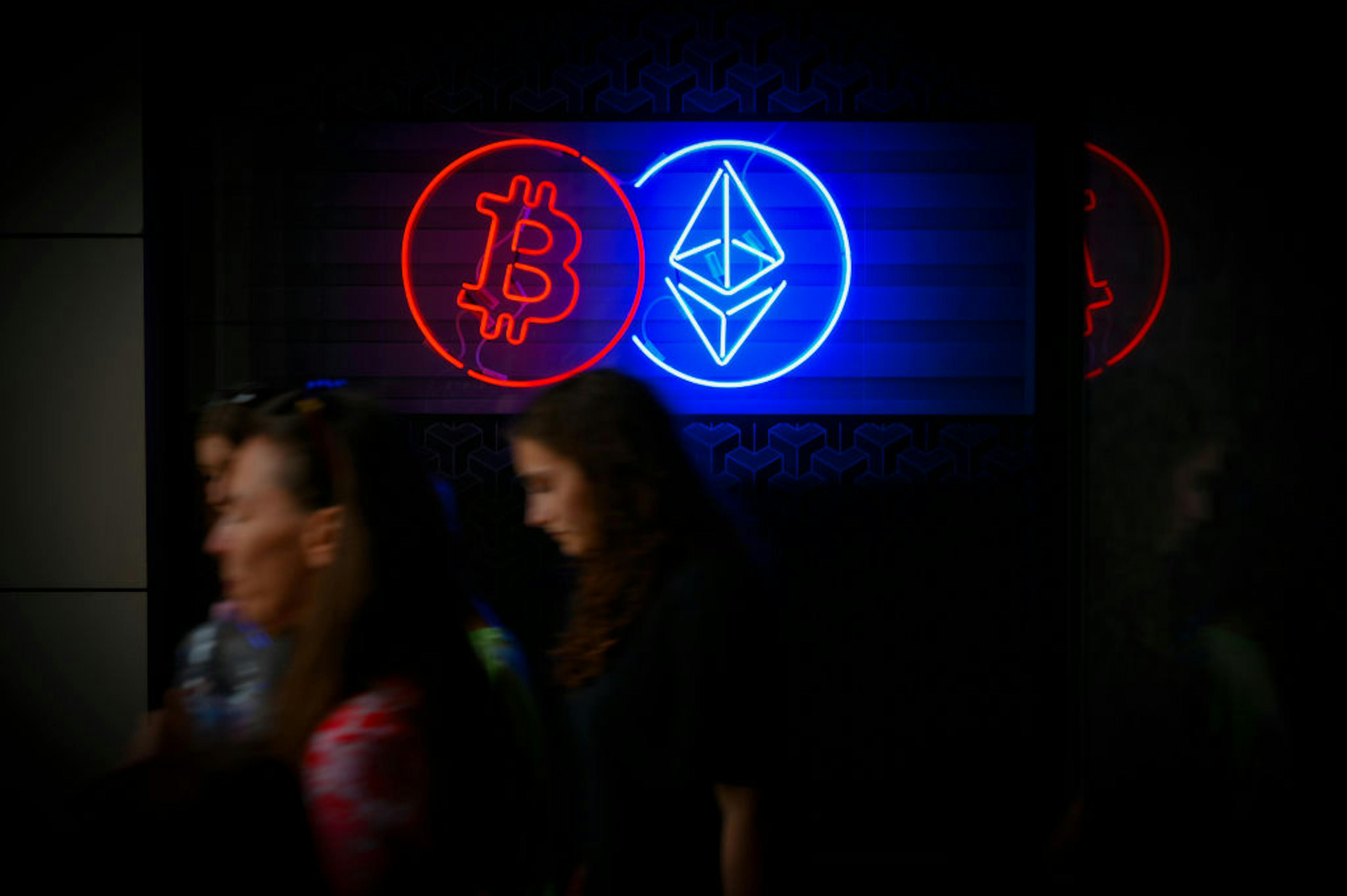 People walk past a neon sign advertising a Bitcoin and Ethereum crypto currency exchange in Warsaw, Poland on 19 May, 2024. 