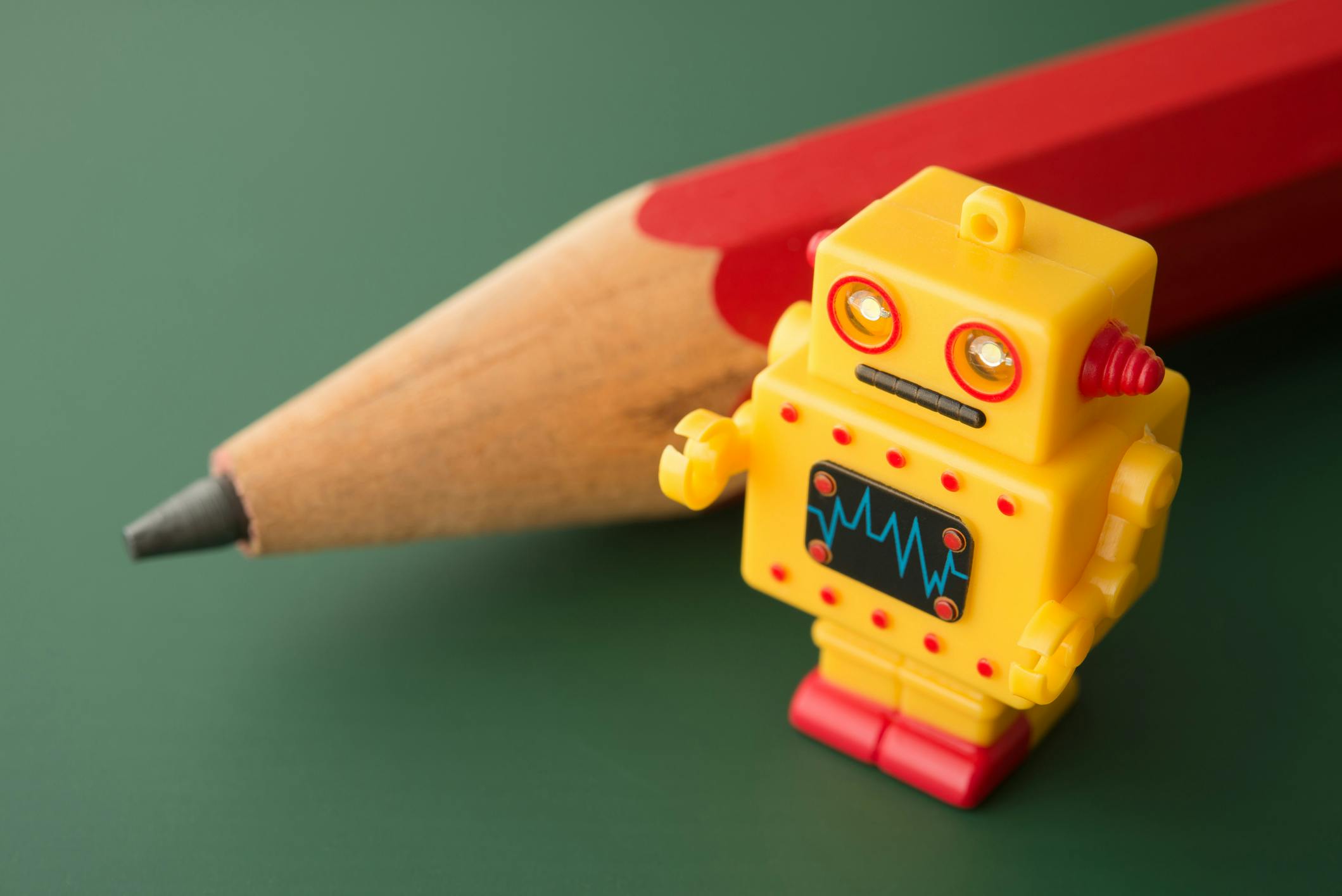Yellow cute robot with red pencil on blackboard background
