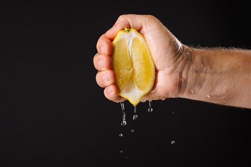 Squeezing fresh lemon juice on dark background, hand squeezing fresh lemon juice close up