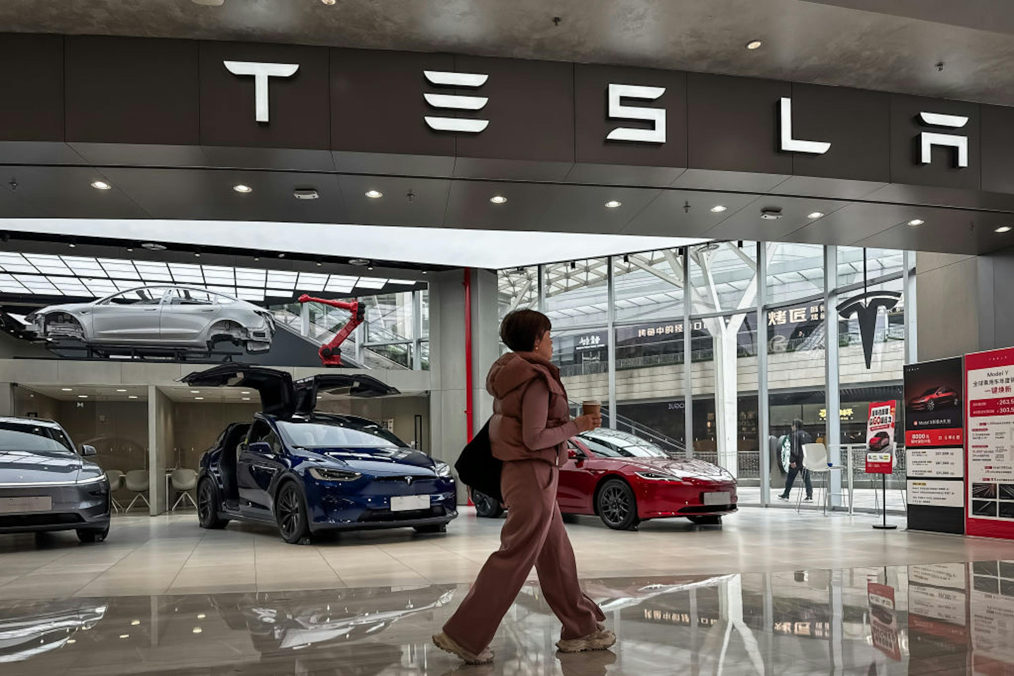 A woman walks past a Tesla with doors open in CHONGQING, CHINA