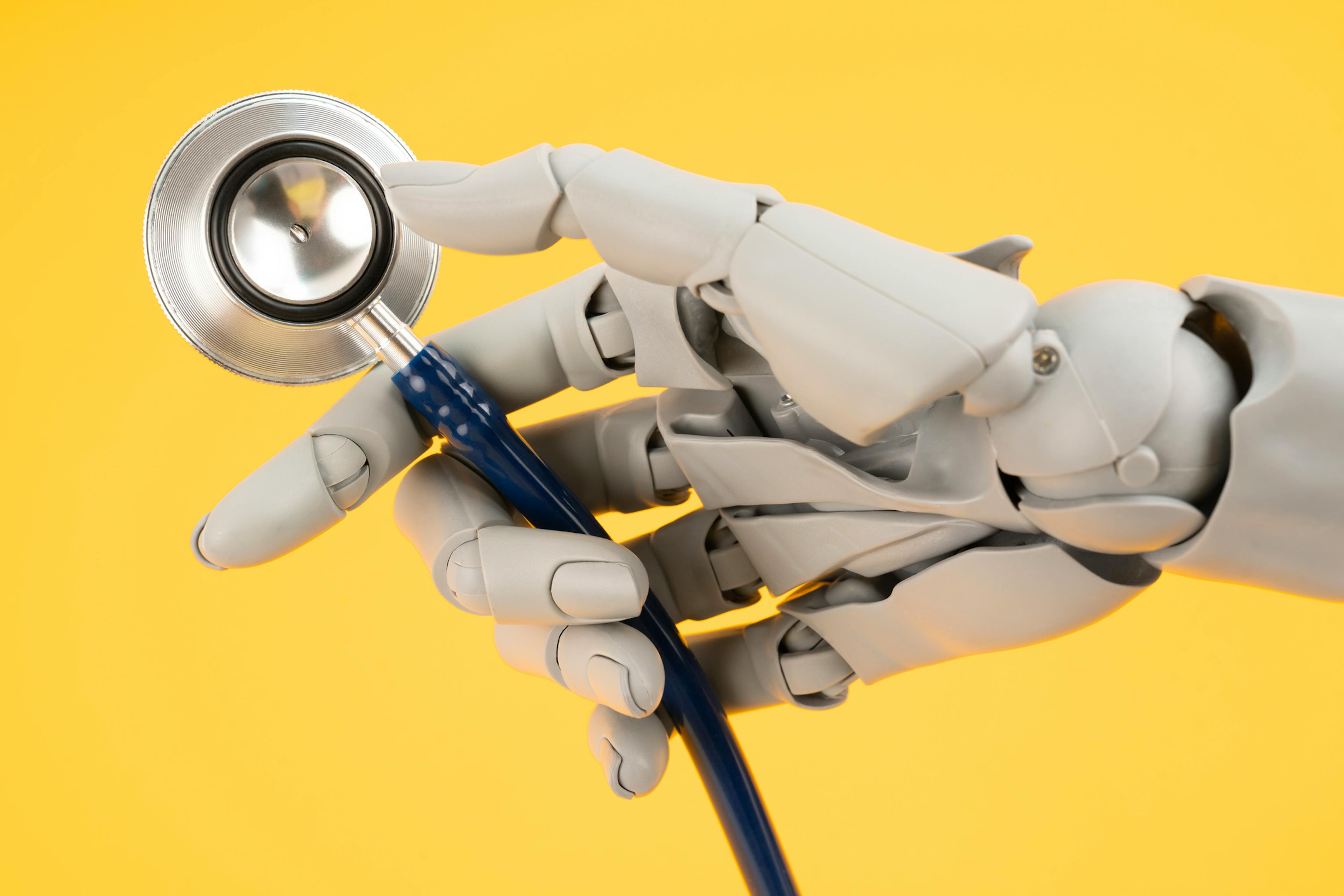 Robot hand toy finger holding medical stethoscope on yellow background, AI and smart technologies in medicine and diagnostic concept.