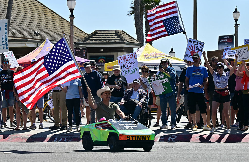 Guy waving an American flag in a tiny Tesla Cybertruck 