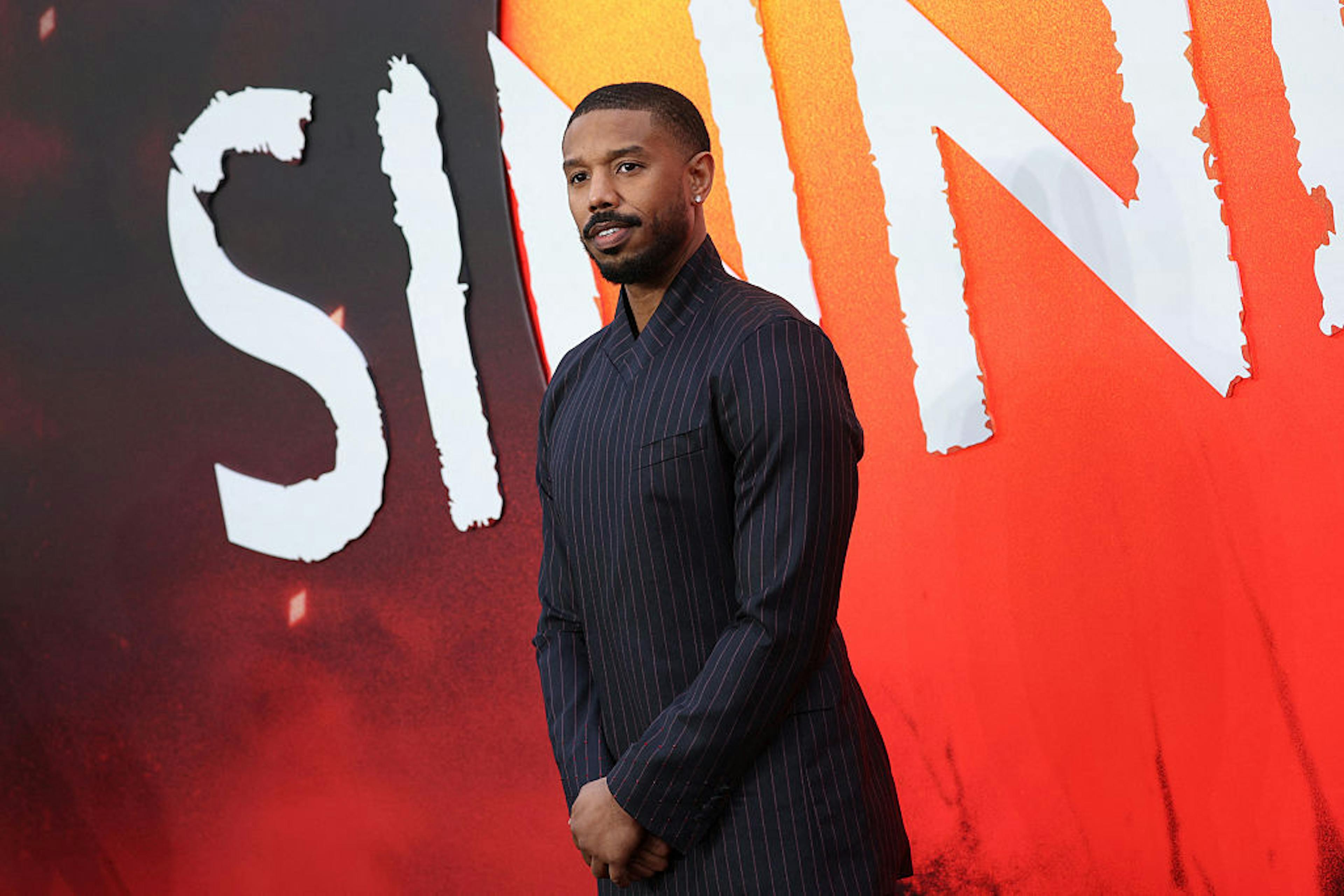 Michael B. Jordan on the red carpet in front of “Sinners” poster