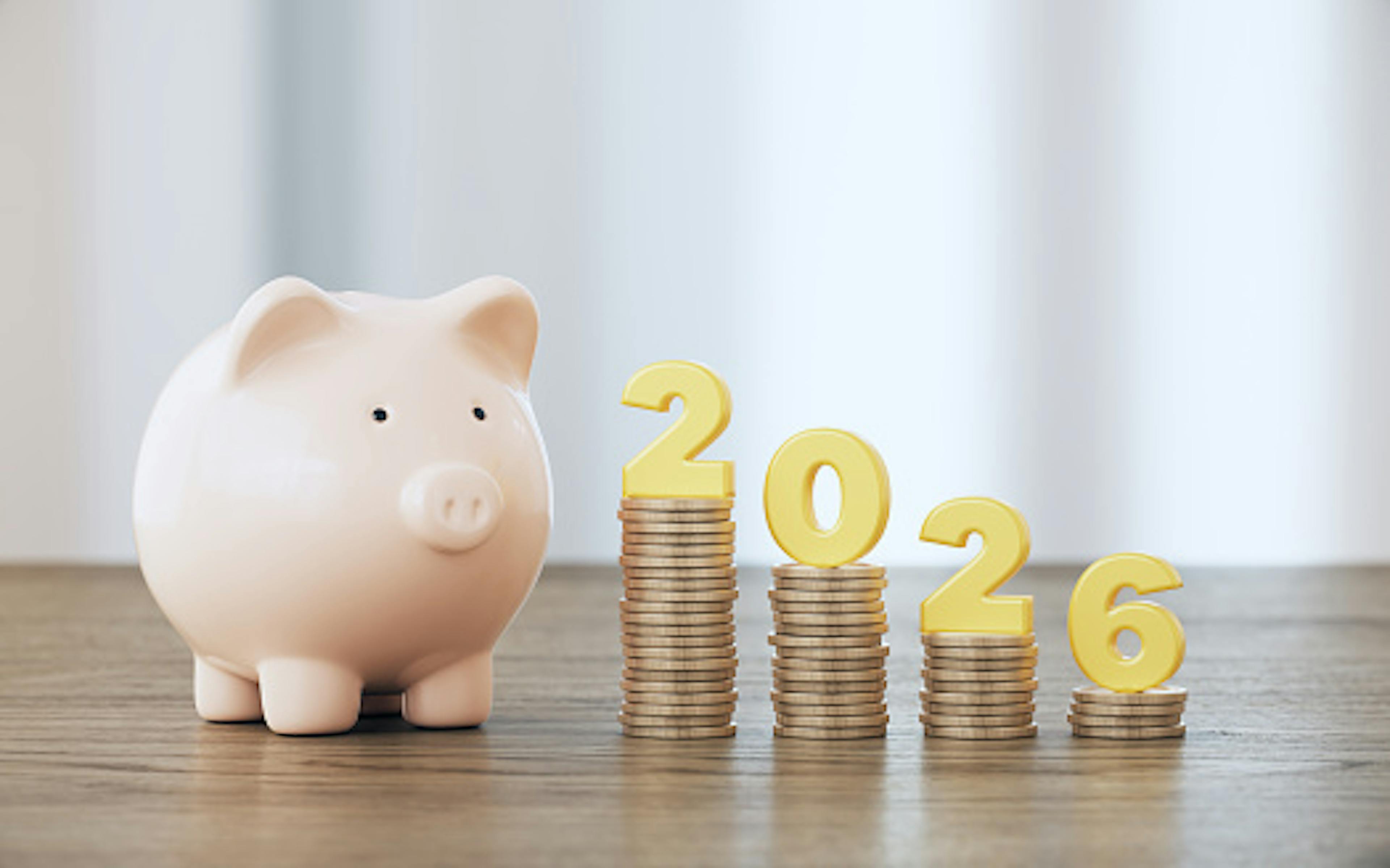 Porcelain Piggy Bank and 2026 Text Sitting on Coin Stack, Over Defocused Wood Background