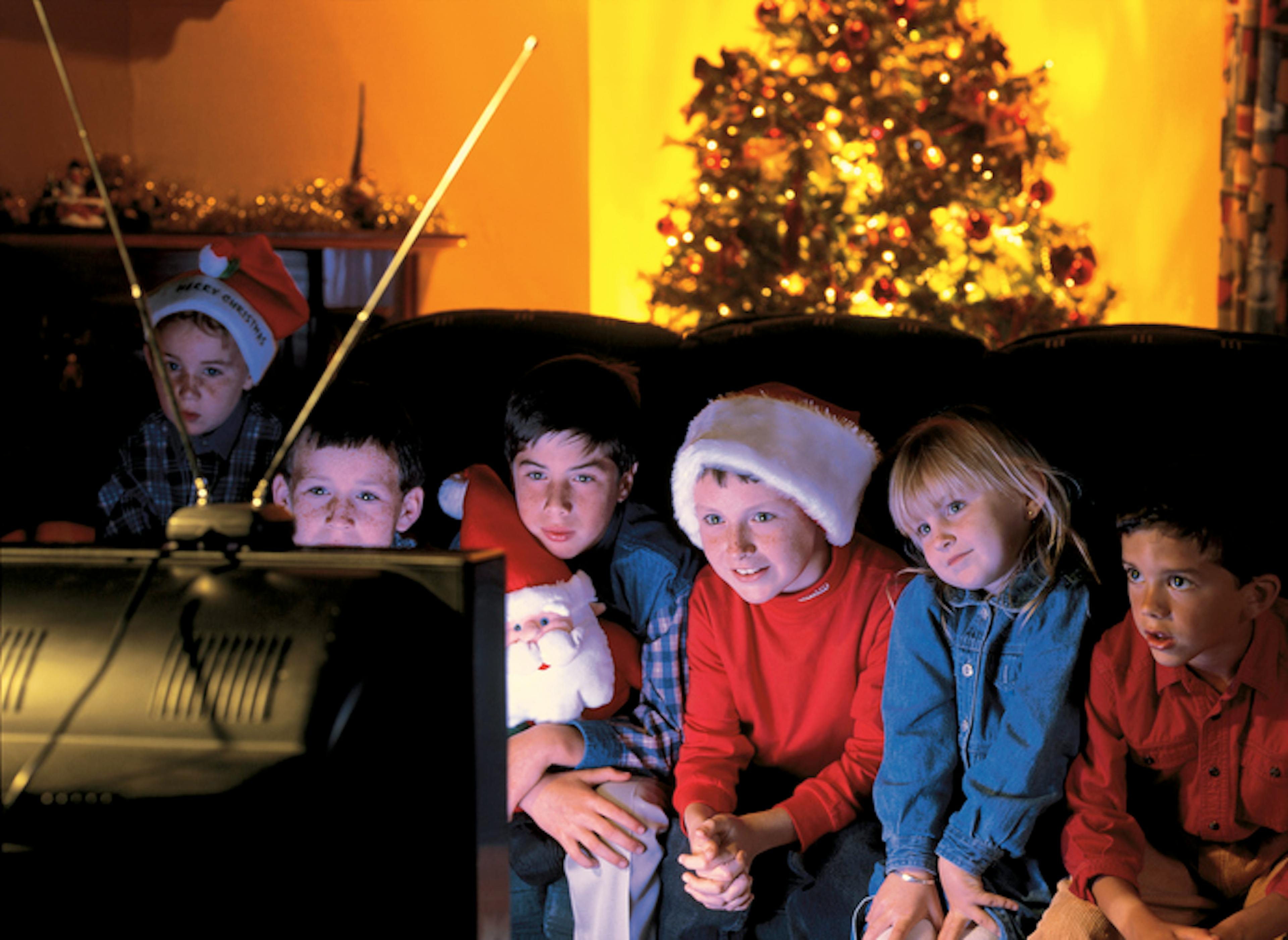 group of children watching television with a Christmas tree behind them