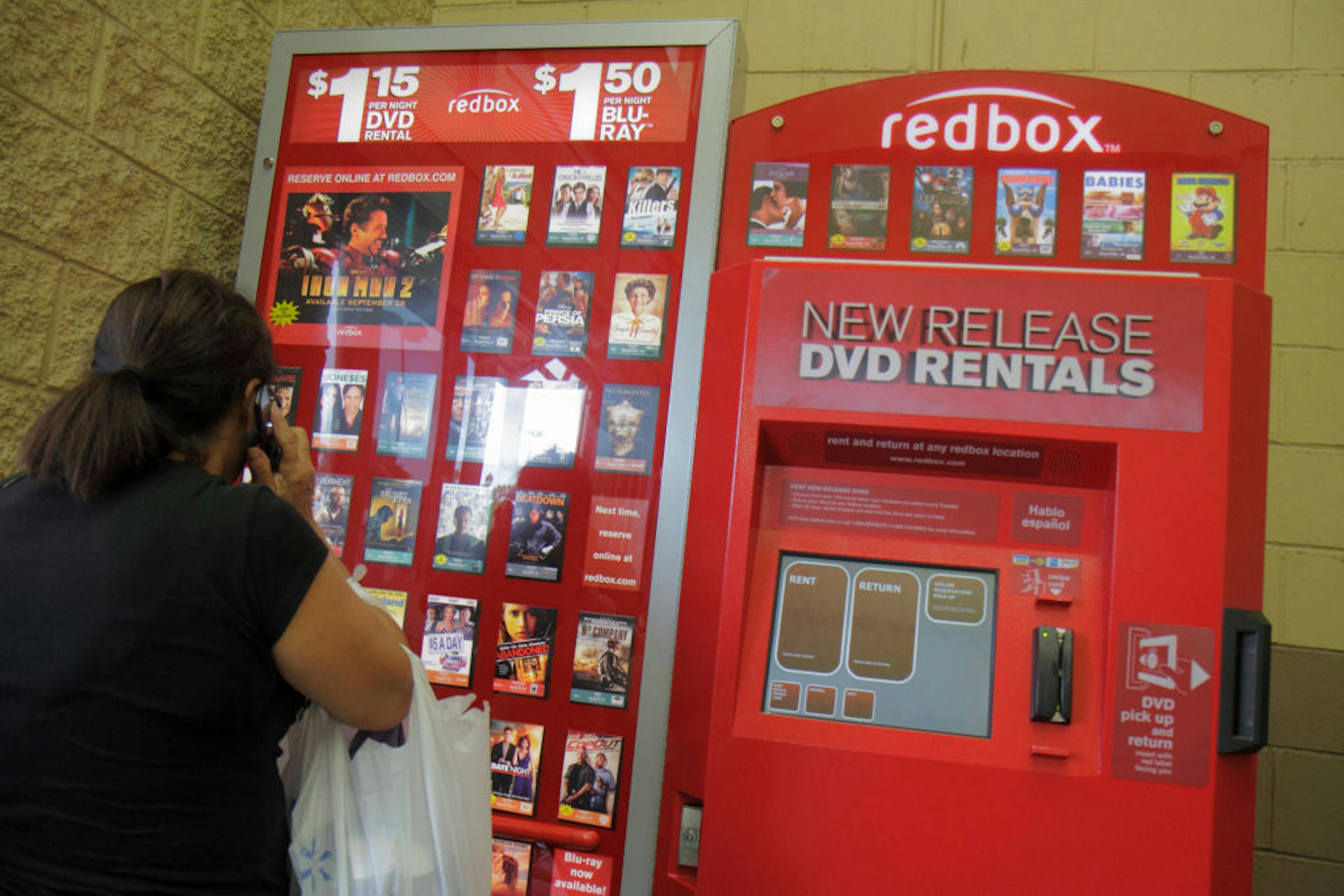 A woman looking at a redbox DVD movie rentals vending machine.